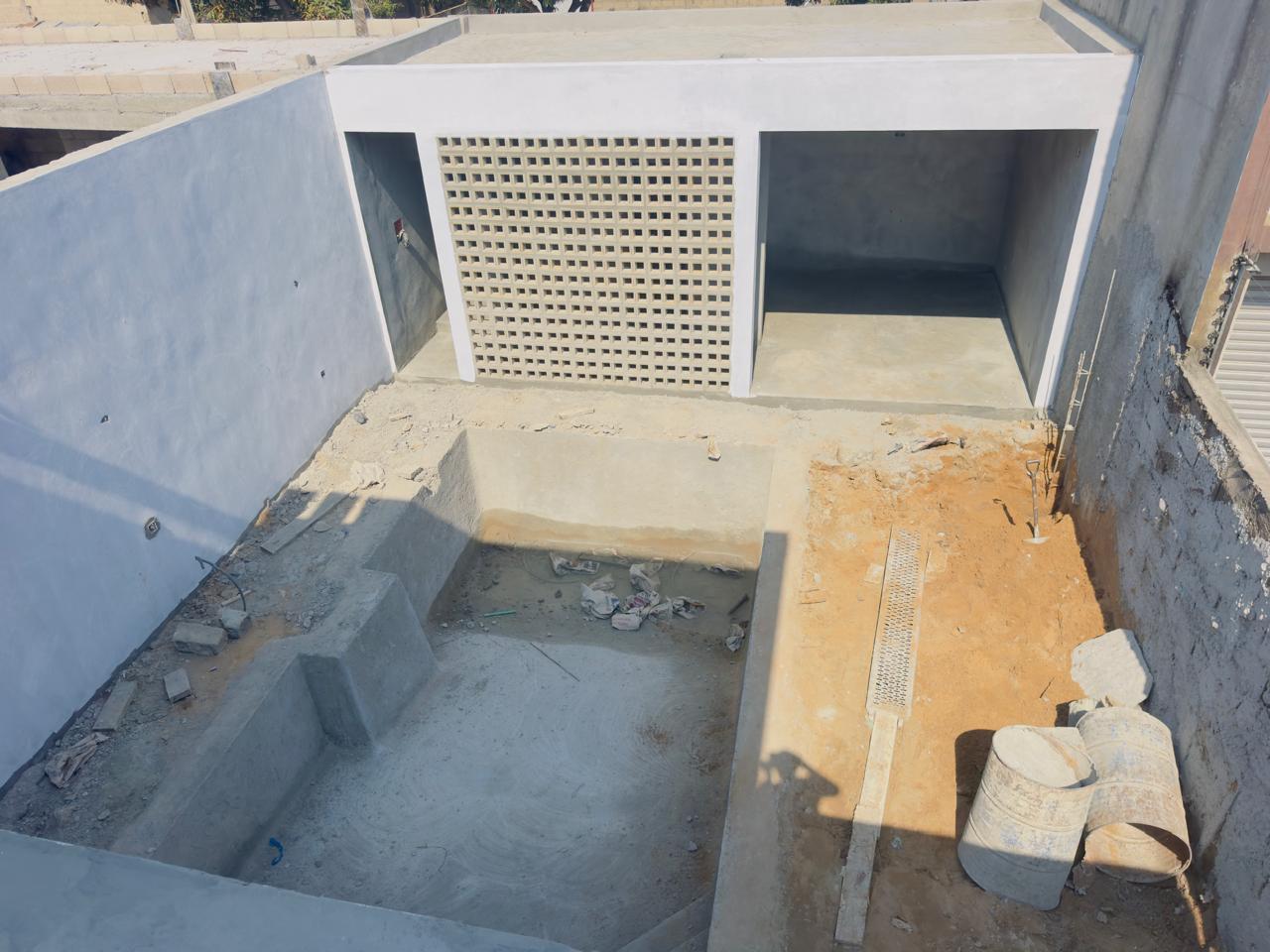 Piscina em obra vista de cima, com a área de lazer ao fundo